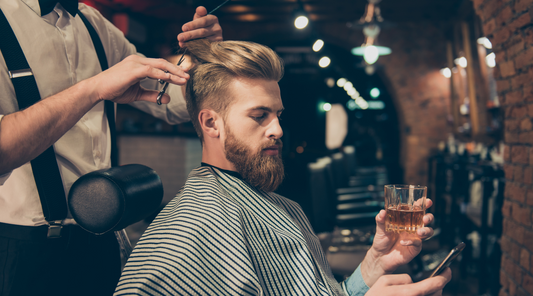 Man getting a stylish haircut while holding a scotch and phone in a barbershop - modern men's grooming and lifestyle